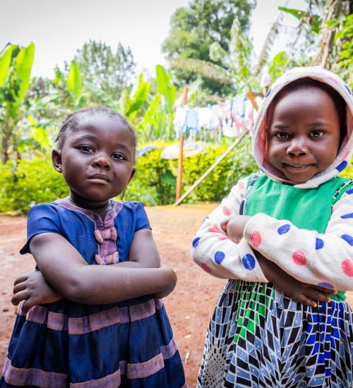 Two African female toddler friends standing outdoors in the village.